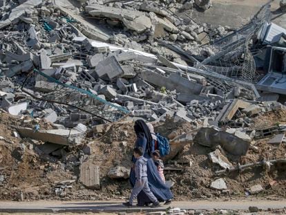 Una mujer camina con sus hijos junto a los escombros de un edificio residencial destruido en el campo de refugiados de Al Nuseirat, en Gaza.