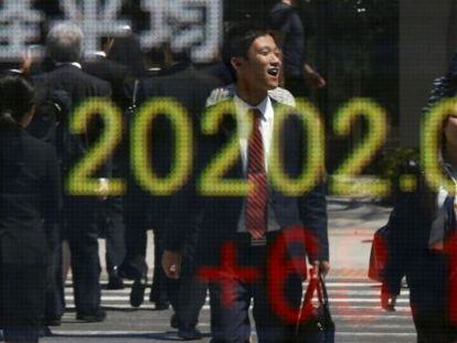 Oficinistas nipones, con su atuendo habitual, pasan por delante de una pantalla de cotizaciones en Tokio.