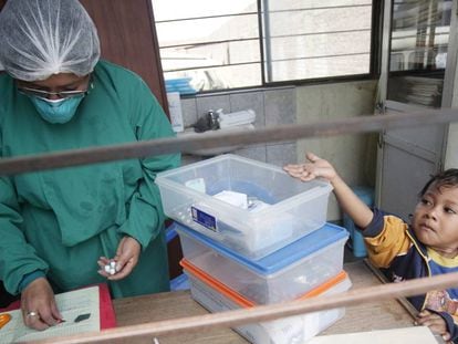 Un ni&ntilde;o con tuberculosis tiende la mano para coger las p&iacute;ldoras de pie junto a una enfermera en un puesto de salud en las afueras de Lima (Per&uacute;)