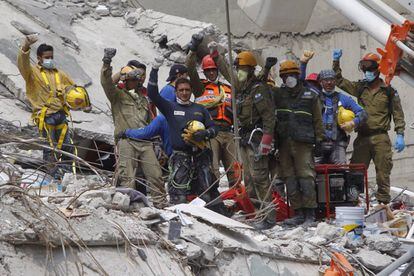 Grupos de rescate de Israel y México levantan los puños como señal de silencio absoluto después de que el perro 'Chichí' y su entrenador reconocieran el sitio donde se hallaba atrapada una persona en un edificio derruido en Ciudad de México.