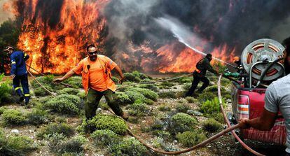 Bomberos y voluntarios intentan extinguir las llamas de un incendio próximo a la ciudad de Kineta, cerca de Atenas.