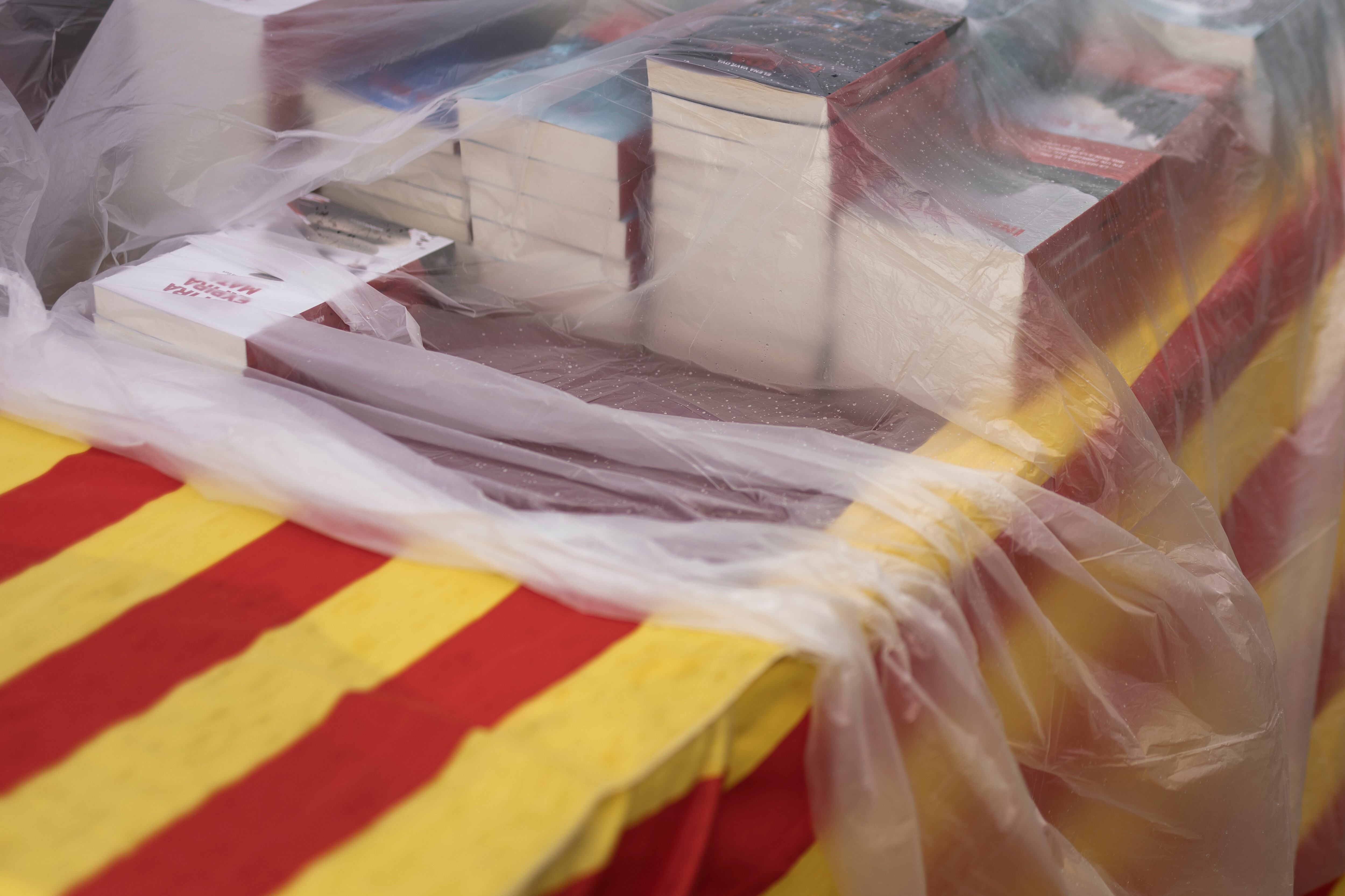 Libros cubiertos con plásticos se apilan en un puesto, para evitar que se mojen con la lluvia, este martes durante Sant Jordi. 
