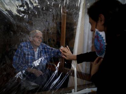 Víctor Tripiana extiende la mano para tocar la mano de su familiar a través de una lámina de plástico en la residencia de ancianos Reminiscencias en Tandil, Argentina, el 4 de abril.