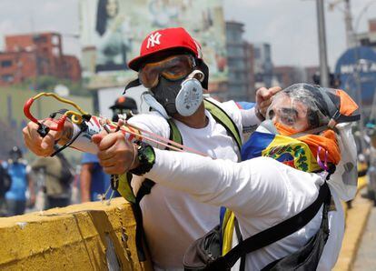 Dos jóvenes opositores lanzan piedras contra los agentes antidisturbios en la estratégica autopista Francisco Fajardo.