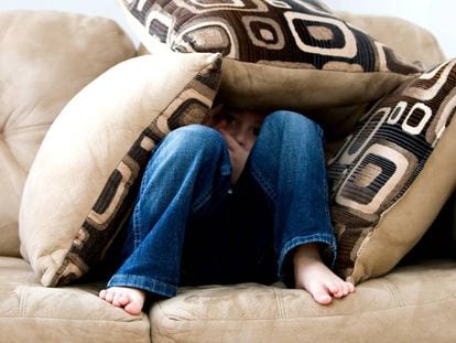 Un niño se esconde entre los cojines del sofá.
