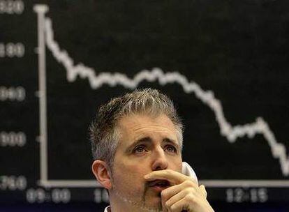 Un empleado de la Bolsa de Francfort habla por teléfono, de espaldas al gráfico que muestra el desplome del índice DAX.