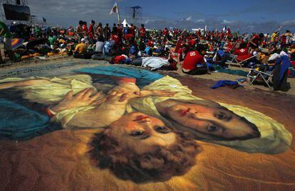 Un numeroso grupo de fieles acampa junto a una imagen gigante de la Virgen Mar&iacute;a y Jesus. en la playa.