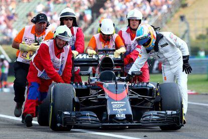 Fernando Alonso (de blanc, a la dreta) ajuda a empènyer el seu cotxe.