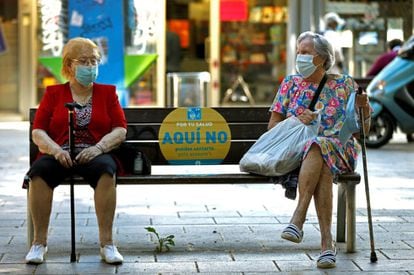 Dos mujeres conversan en un banco de L'Hospitalet (Barcelona). La duración de uso de mascarillas dependerá del criterio del Ministerio de Sanidad en función de cómo evolucione la pandemia durante la desescalada.