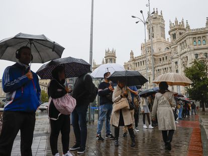 Varias personas se protegen del diluvio frente al Palacio de Cibeles, este jueves en Madrid.