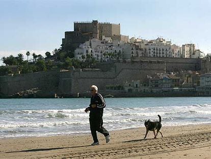 Un jubilado corre con su perro por la playa de Peñíscola.