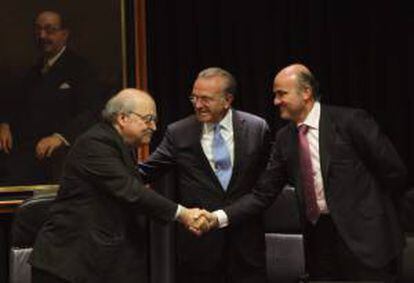 El ministro de Economía, Luis de Guindos (d), y el presidente de La Caixa, Isidro Fainé (c), saludan al conseller de Economía de la Generalitat, Andreu Mas-Colell, tras la firma.