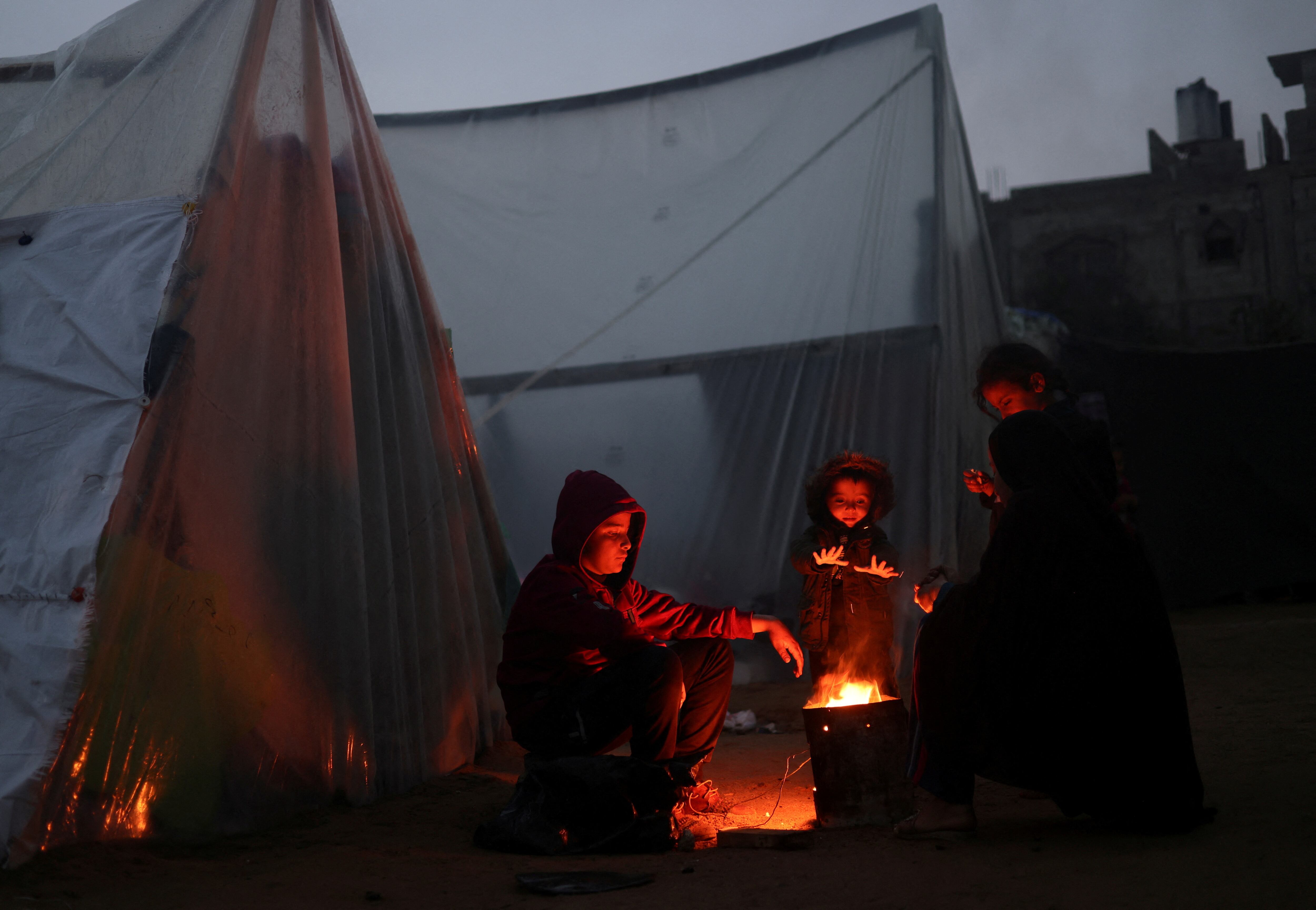 Desplazados palestinos en un campamento de Rafah, al sur de la franja de Gaza, se calientan al fuego en un día de lluvia.