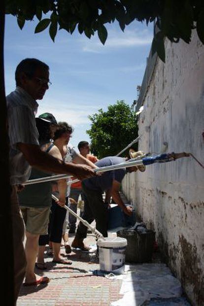 Unos vecinos encalan el muro del polideportivo en Higuera de la Serena.