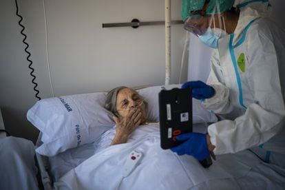 La enfermera Marta Fernández sostiene una tableta sobre el pecho de María Teresa Argullos Bove, de 94 años, para que pueda hablar con su hermana, sus hijos y sus nietos desde su cama en el hospital del Mar en Barcelona, el 18 de noviembre de 2020.