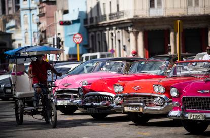 Un bicitaxi pasa frente a varios coches clásicos que esperan clientes, el 27 de enero, en el Parque Central de La Habana, Cuba.