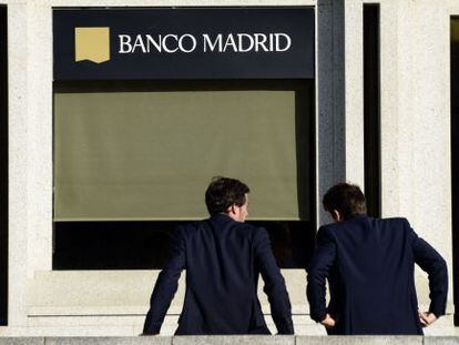 Dos hombres esperan en la puerta de la sede de Banco Madrid.