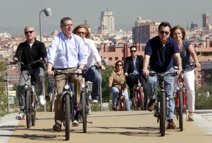 Gallardón da un paseo con su equipo en bicicleta eléctrica por el río.