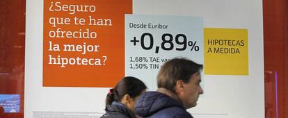 Una pareja pasea junto a un cartel de comercialización de hipotecas.