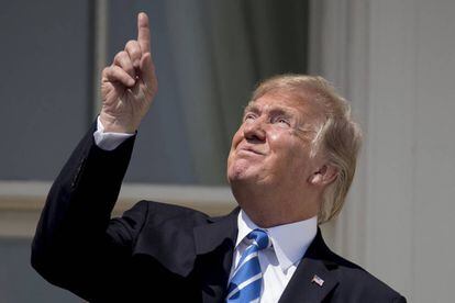 Trump señala al sol mientras lo observa sin gafas.