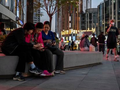 Un grupo de mujeres miran sus móviles en una área central de Pekín, China.