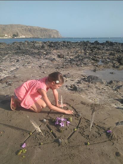 Una niña hace su mandala en la playa con piedras, plumas y flores dibujadas en El Médano.