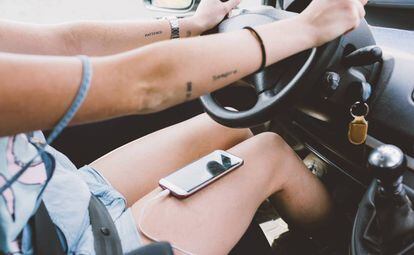 Una chica conduce con el móvil en las piernas.