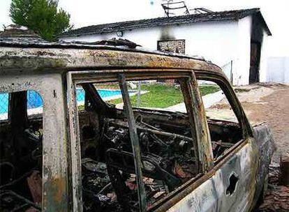 El coche calcinado de Javier Bernuy, <i>El Calvo,</i> y al fondo, la casa donde vivía con parte de su familia y que también fue incendiada por vecinos.