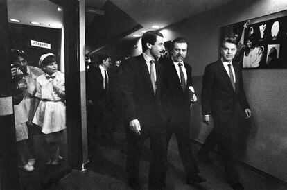 Aznar, Mariñas y González caminan por un pasillo de Tele 5 hacia el plató donde se desarrollará el segundo debate electoral de 1993. Varios trabajadores de la televisión contemplan la escena con expectación.
