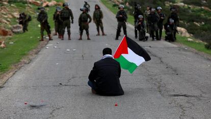 Un manifestante con una bandera palestina se sienta frente a las fuerzas israelíes durante una protesta contra los asentamientos israelíes en febrero.