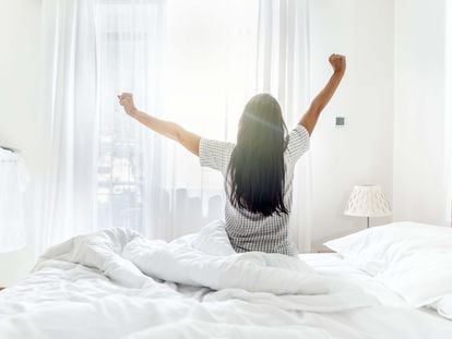 Una joven se levanta y despierta de la cama con los primeros rayos de sol.