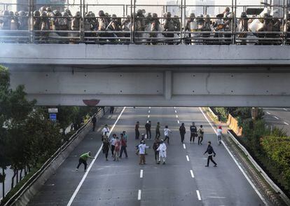 Los manifestantes lanzan piedras a los oficiales de la policía, concentrados sobre el puente, durante los disturbios en Yakarta, este miércoles.
