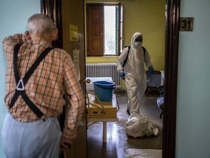 Un hombre espera en el exterior de su habitación en una residencia de mayores mientras los bomberos trabajan en la desinfección.