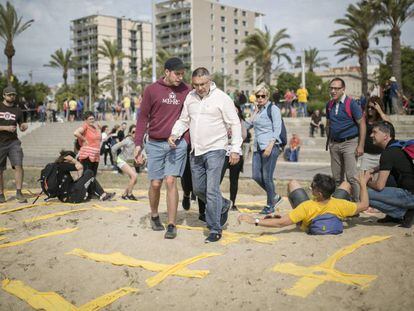 Dos hombres intentan pisar cruces amarillas con toallas en la playa de Mataró este domingo.