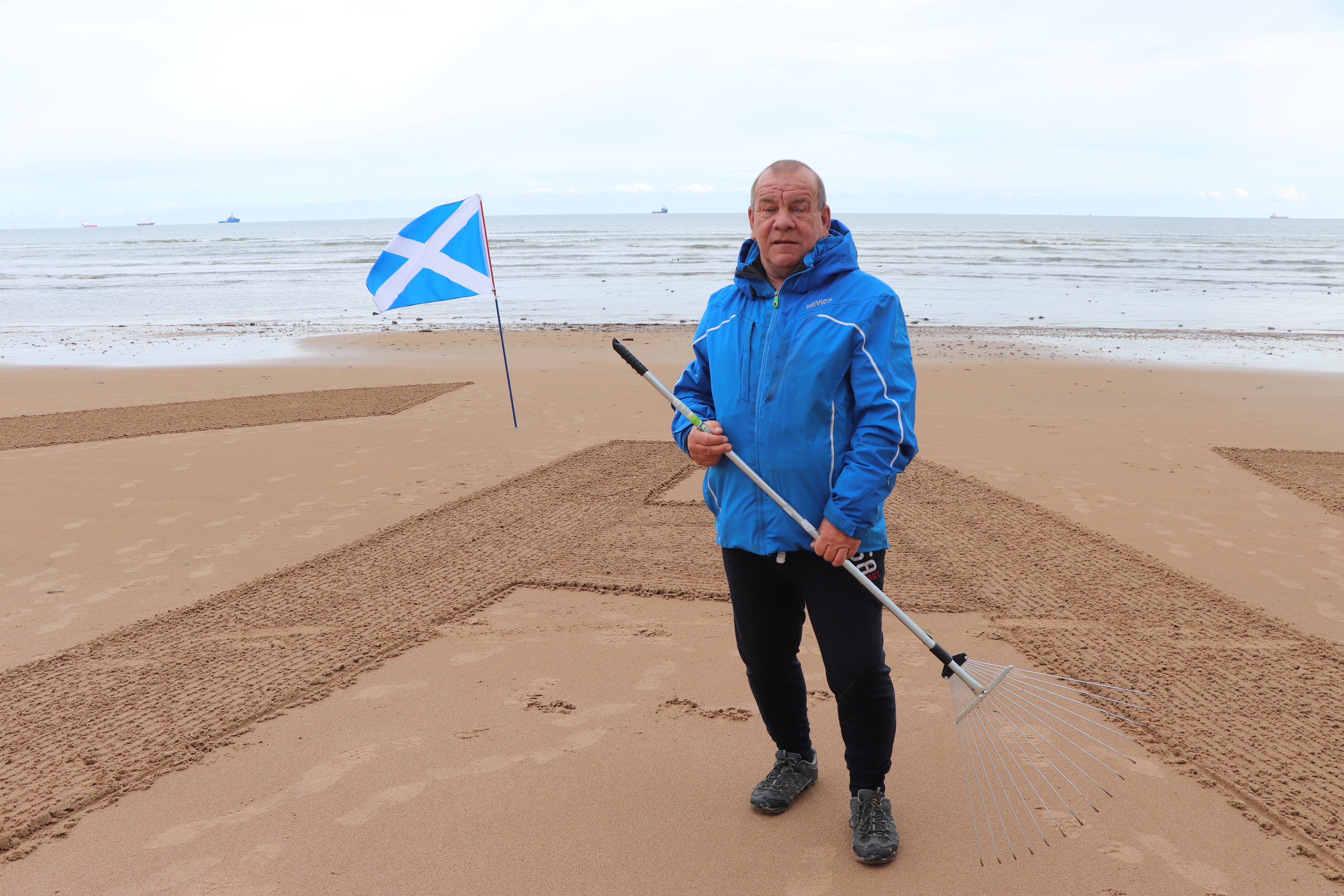 Dougie Bogie escribe con un rastrillo las letras del partido Alba, en la playa de Aberdeen.