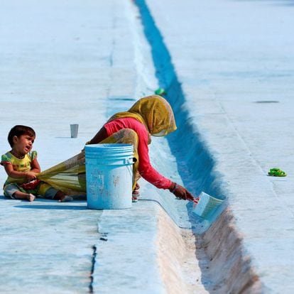 Una mujer pinta el hormigón de un estanque mientras un niño tira de su ropa, en Delhi (India), en 2019.