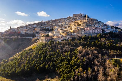 Sant’Agata di Puglia, conocido como el “balcón de Apulia”, mantiene intacto el misterio de una aldea medieval de montaña con un laberinto de ‘trasonne’ (callejones) que se extienden hasta el castillo situado en lo alto. Las vistas desde la plaza principal dejan sin aliento. Y por la noche, de lejos, el pueblo parece un árbol de Navidad iluminado.
Sant’Agata está en el interior, en el corazón de Apulia, y es uno de esos lugares fascinantes, donde un simple paseo es suficiente para despertar nuestra curiosidad. Desde sus 800 metros de altitud se goza de unas vistas amplias y emocionantes del valle del río Carapelle y hasta el bajo Tavoliere, desde el promontorio del Gargano hasta el golfo de Manfredonia. El lugar es espectacular, sobre todo hacia el atardecer, cuando se van encendiendo lentamente las luces de las casas y de las calles, que convergen en la plaza y, más a lo alto, en el castillo. En la Piazza XX Settembre hay una hermosa terraza panorámica adornada con macetas, que es como un balcón con un paisaje ilimitado de campos y bosques coronado por el perfil inconfundible del monte Vulture. Resulta agradable (aunque un poco agotador) recorrer el pueblo medieval, entre pequeñas casas de tejados uniformes de terracota, descubriendo los símbolos heráldicos y los hermosos portales de piedra tallada que ennoblecen las fachadas con cariátides, escudos, máscaras y motivos vegetales.
Hay otros encantos a descubrir en la naturaleza que rodea Sant’Agata: en el bosque de Serbaroli, a lo largo de la carretera de Accadia, se alza el megalito llamado Pietra di Sandu Linze (San Lorenzo) y su pozo sagrado.