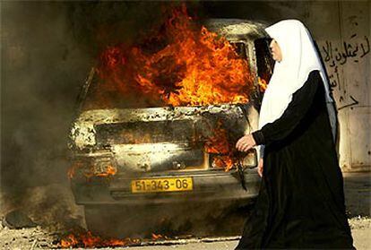 Una mujer palestina pasa ante un coche en llamas durante los enfrentamientos con soldados israelíes en Nablús.