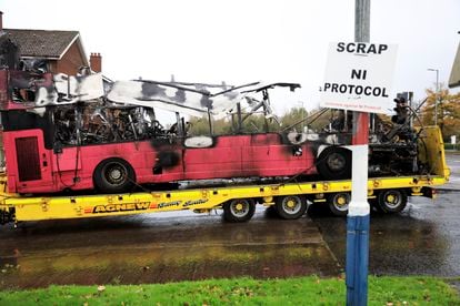 Los restos del autobús incendiado en Belfast, este lunes. Frente al vehículo, un cartel exige la retirada del Prtocolo de Irlanda del Norte