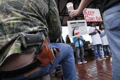 Un hombre armado observa en Seattle a manifestantes que reclaman que se prohíba el acceso a personas con armas en establecimientos públicos.