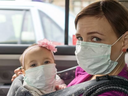 Una madre y su bebé con mascarilla en un coche.