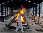 A priest wearing personal protective equipment (PPE) walks in front of the body of a person who died of the coronavirus disease (COVID-19), as he collects woods to make a funeral pyre at a crematorium in New Delhi, India, July 3, 2020. REUTERS/Anushree Fadnavis