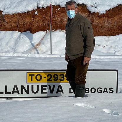 Un vecino de Villanueva de Bogas (Toledo) frente al rótulo de acceso al pueblo, semicubierto de nieve.