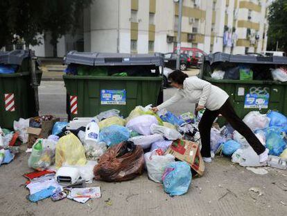 Una mujer deposita una bolsa de basura frente a los contenedores abarrotados en una calle de Jerez.