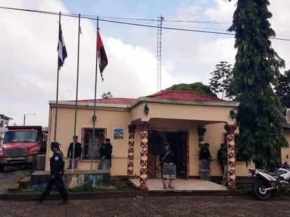 Fuerzas policiales del gobierno de Daniel Ortega resguardan un edificio, con la bandera sandinista izada junto a la bandera nicaragüense.