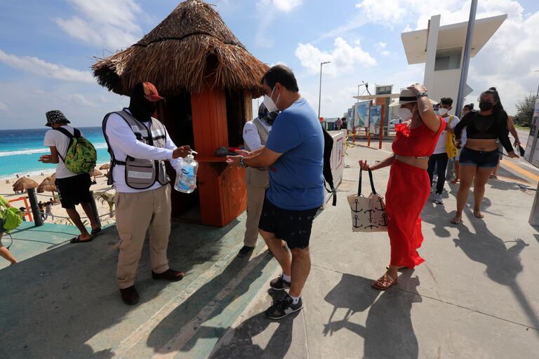 Un hombre reparte líquido desinfectante a turistas en la playa en Cancún, en enero.