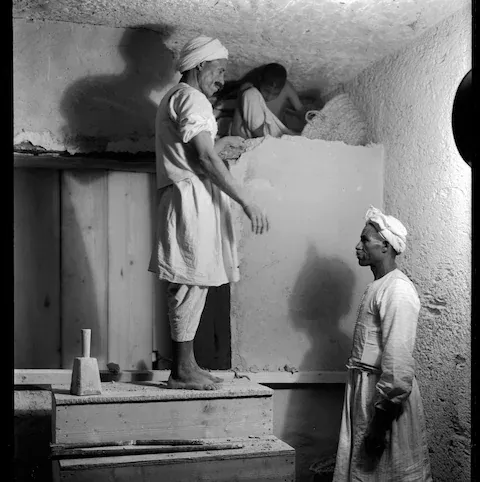 Tres trabajadores egipcios desmontan el muro entre la antecámara y la cámara funeraria de la tumba de Tutankamón.