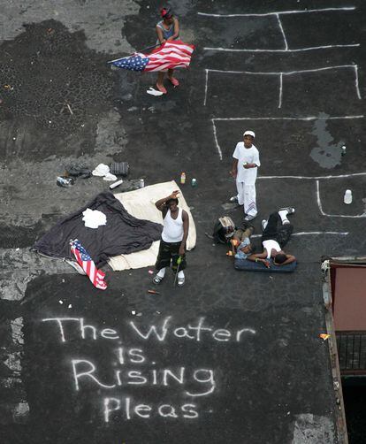 Un grupo de residentes en Nueva Orleans esperan a ser rescatados en la azotea de un edificio, con un mensaje escrito en el suelo: "El agua está subiendo. Ayuda".