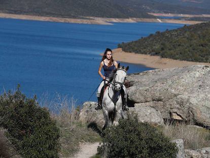 Una joven pasea a caballo por El Berrueco. Al fondo, el embalse de El Atazar.