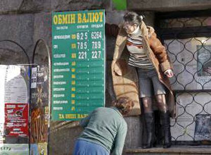 Empleados de una oficina de cambio de moneda cuelgan un cartel con tasas, en Kiev, Ucrania. EFE/Archivo